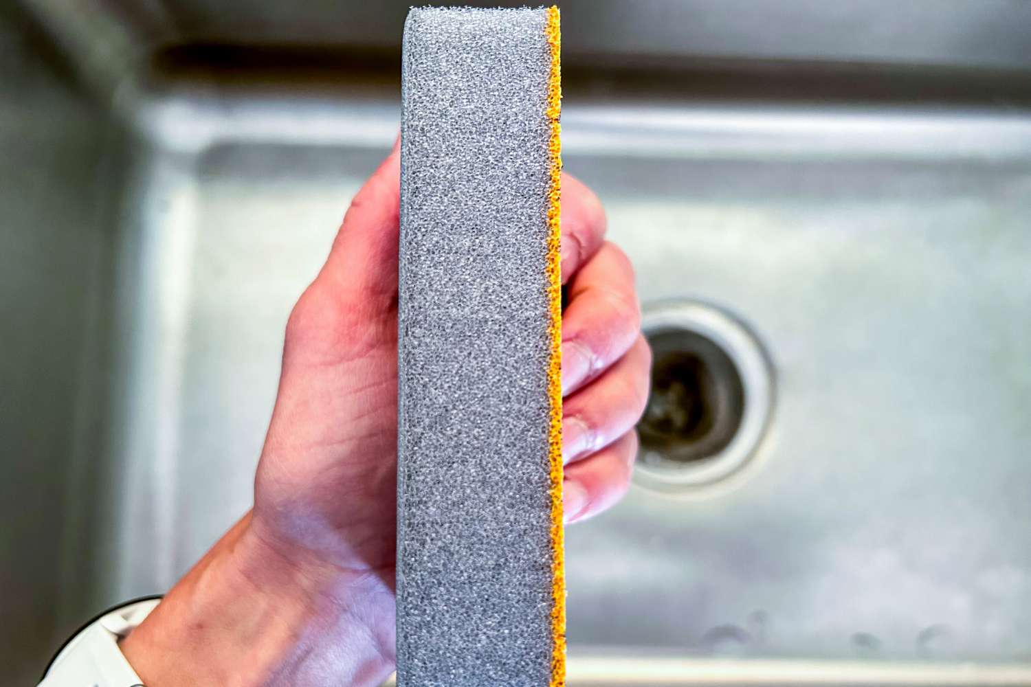 A Skura dishwashing sponge being held over a kitchen sink