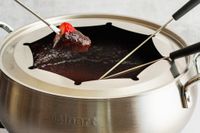 A strawberry being dipped into chocolate fondue in the Cuisinart fondue pot.
