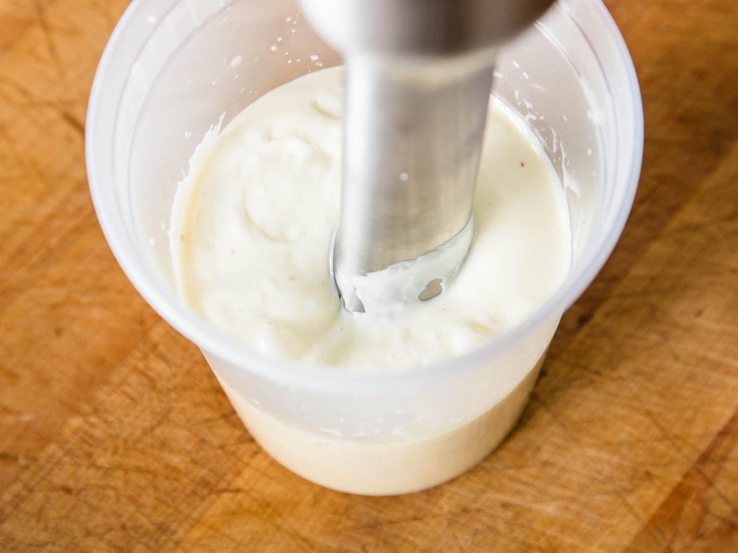 Using an immersion blender to make whipped cream in a plastic container.