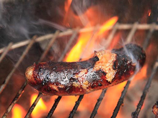 A sausage on the grill that has burnt slightly on the outside and burst open