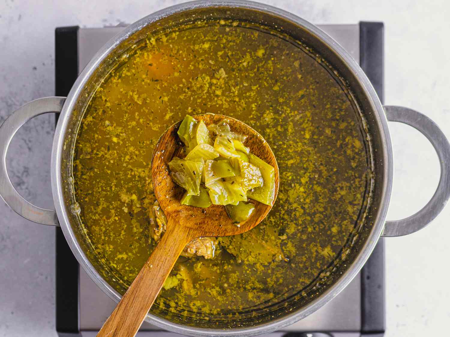 A wooden spoon lifting softened vegetables out of a pot