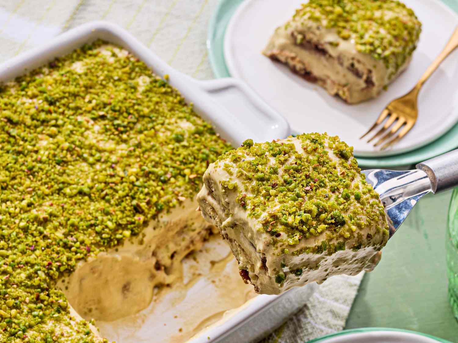 Pistachio tiramisu in a dish a serving being lifted with a spatula revealing layers