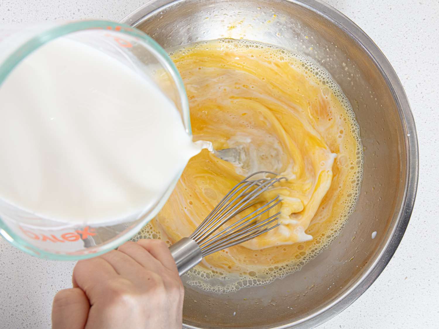 Overhead view of adding milk to mixing bowl