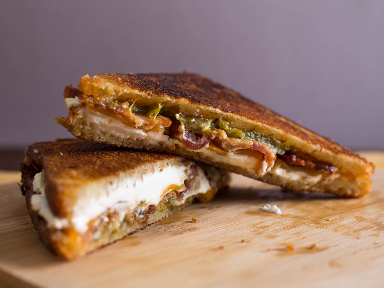 A jalapeño popper grilled cheese sandwich, halved and arranged on a cutting board.