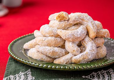 A stack of crescentshaped cookies dusted with powdered sugar arranged on a green plate placed over a festive napkin
