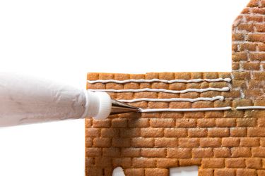 Piping homemade royal icing onto a piece of gingerbread for a gingerbread house.