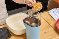 A person pours popcorn kernels into the Dash Hot Air Popcorn Maker
