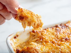 A closeup of a hand holding a scoop of baked dip with melted cheese from a dish