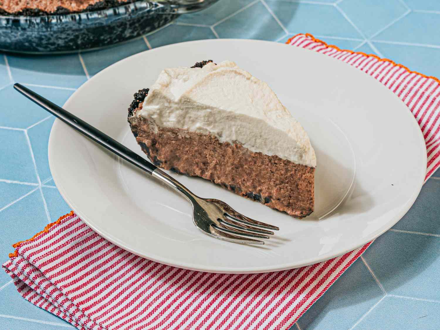 A slice of pie with whipped topping served on a plate with a fork on a striped napkin