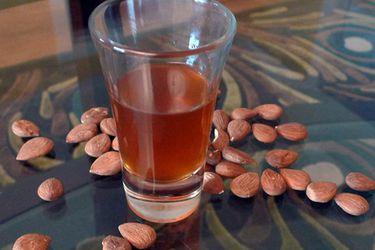 A flared shot glass of DIY amaretto, surrounded by whole raw almonds.