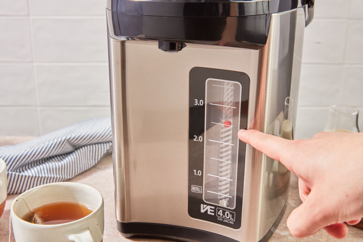 A finger pressing a water level indicator on a countertop water boiler