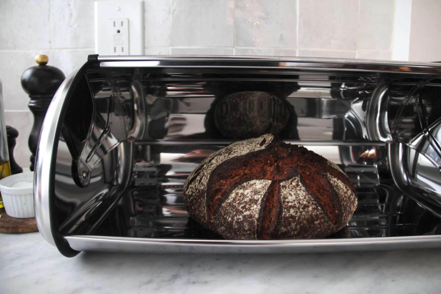 A loaf of bread inside a reflective bread box, kitchen countertop in the background