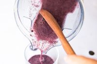 Pouring a purple smoothie from a blender into a glass with a wooden spoon