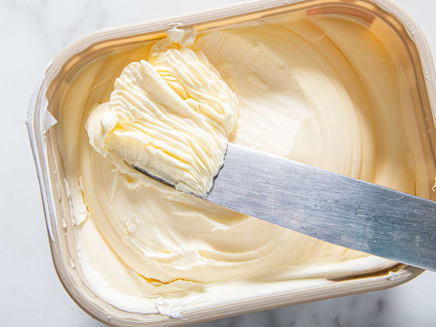 A knife spreading margarine from a container focused on the creamy texture and spreading motion