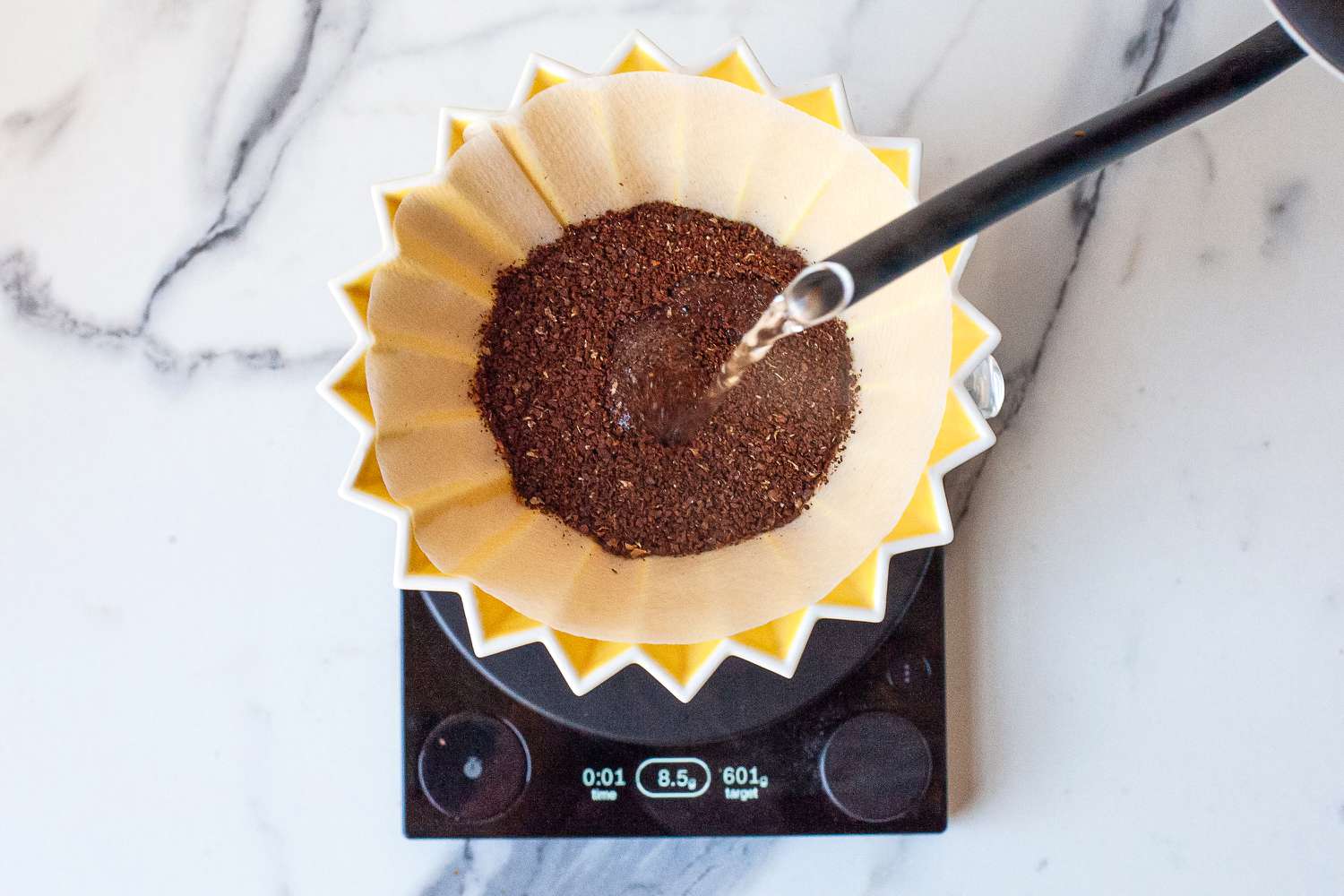 Pouring water over coffee grounds in a pour-over coffee maker's filter set on a scale.
