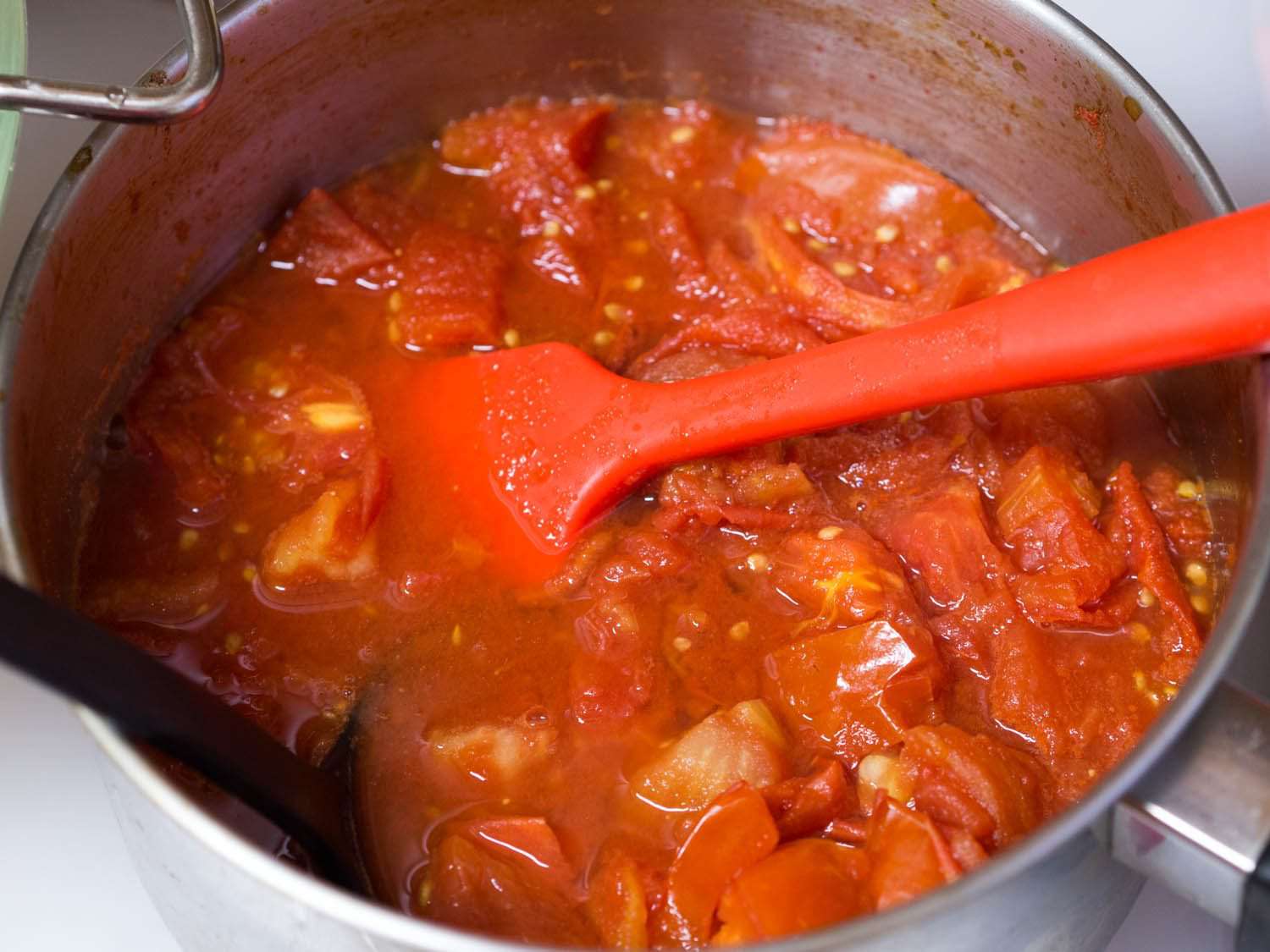 Pot of tomato sauce stirred by a red spatula.