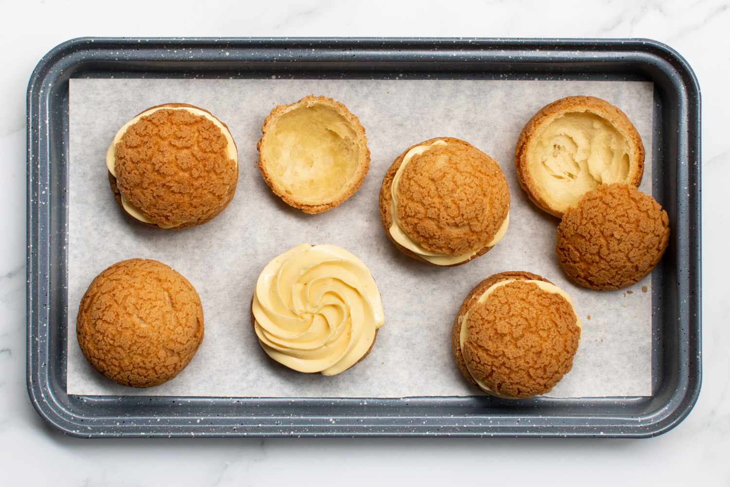 An overhead of six hollowed out puffs that have been filled with filling and are resting on a baking sheet. 