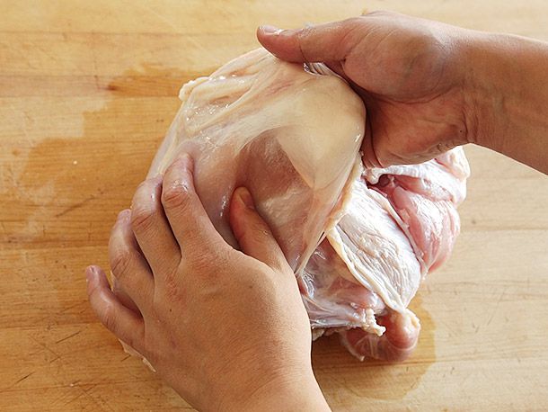 Using two hands to gently lift up and remove the turkey skin from a whole bone-in turkey breast.