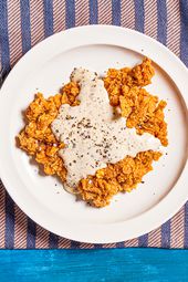 Chicken fried steak on a white plate on a purple and pink stripped towel on a blue backdrop