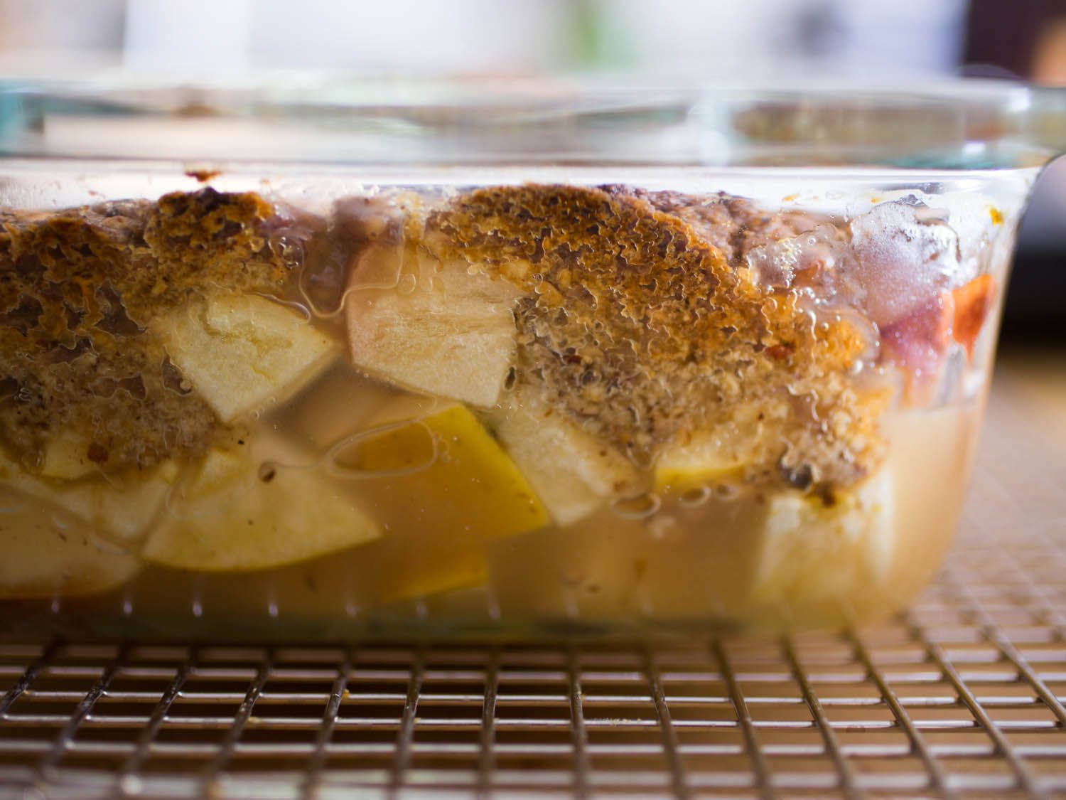 Close-up side view of a glass baking dish full of apple chunks and crumble topping, on a wire rack.