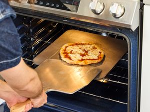 A person transferring a baked pizza from the pizza steel onto a pizza peel.