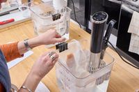 A person secures a sealed bag to the side of a container holding the Instant Accu Slim Sous Vide Immersion Circulator