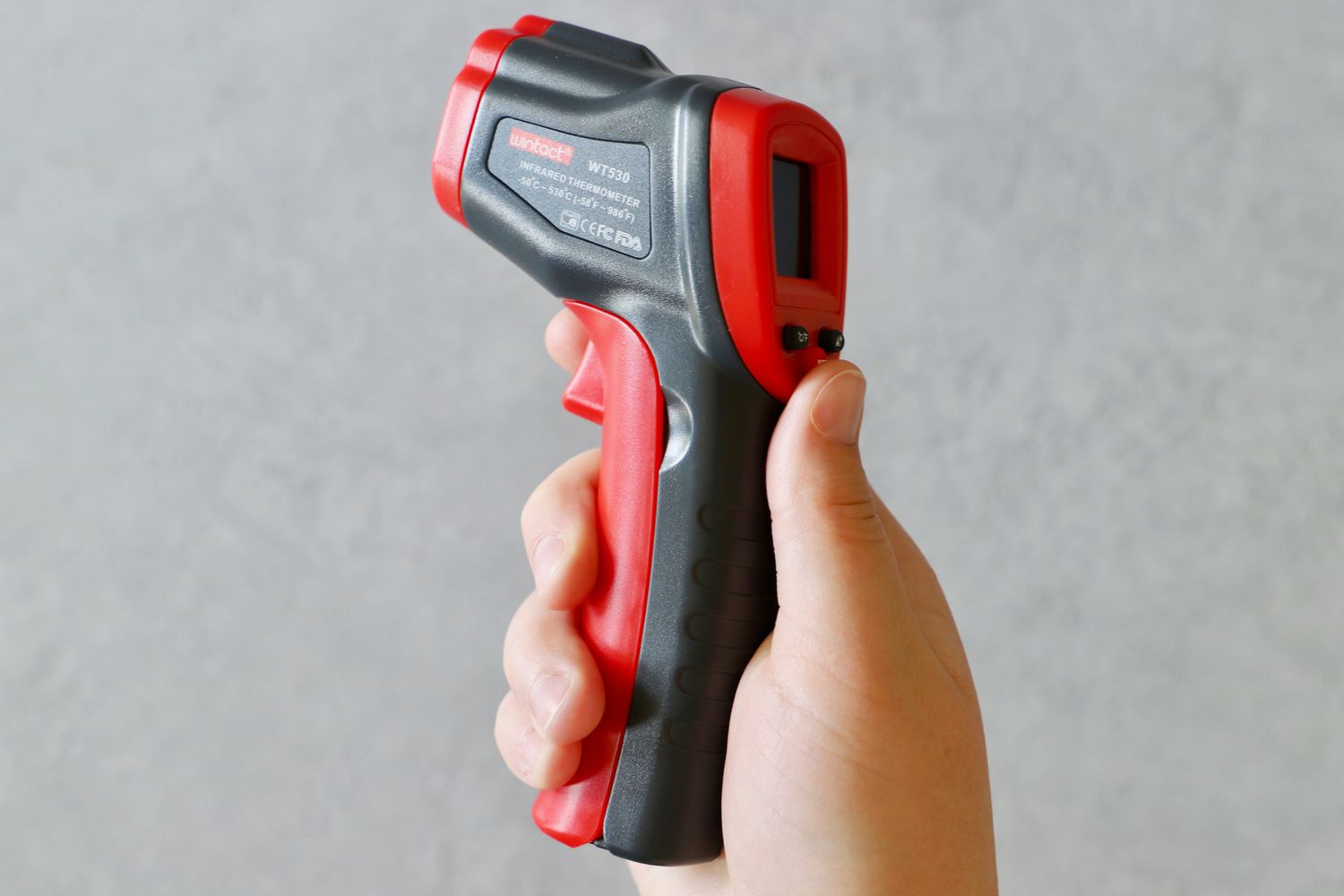 a black and red infrared thermometer in a person's hand