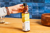 A hand holding a bottle of white sesame oil on a kitchen counter