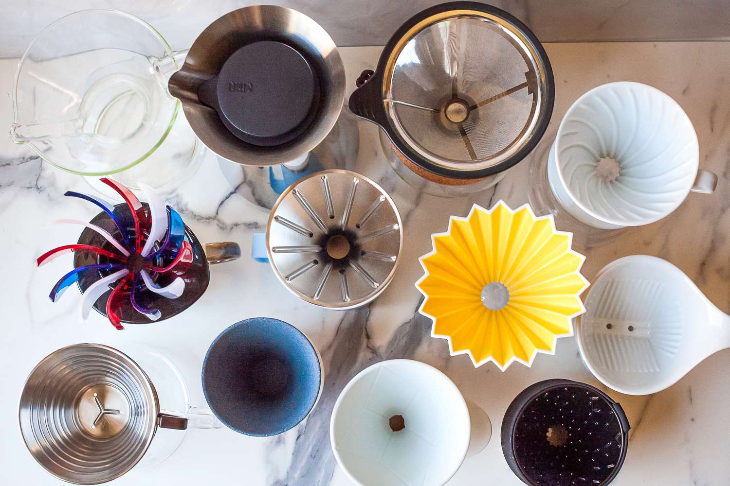Various coffee drippers of different designs and materials on a marble surface