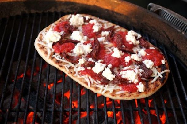 Pizza with toppings grilling over hot coals 