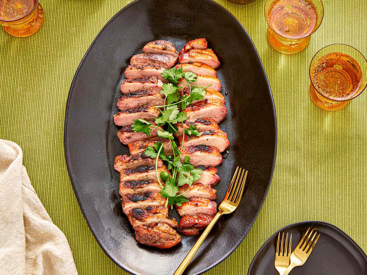 A plate of sliced smoked duck breasts garnished with herbs presented on a table with drinks and dinnerware