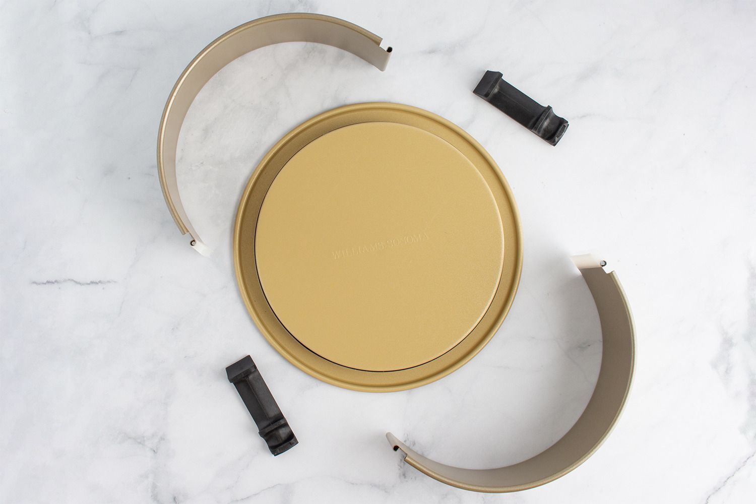 The Williams Sonoma springform pan disassembled on a marble kitchen countertop.