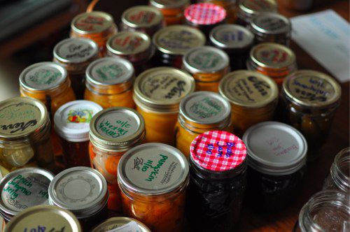 A table covered in glass jars with lids, all containing different things being pickled.