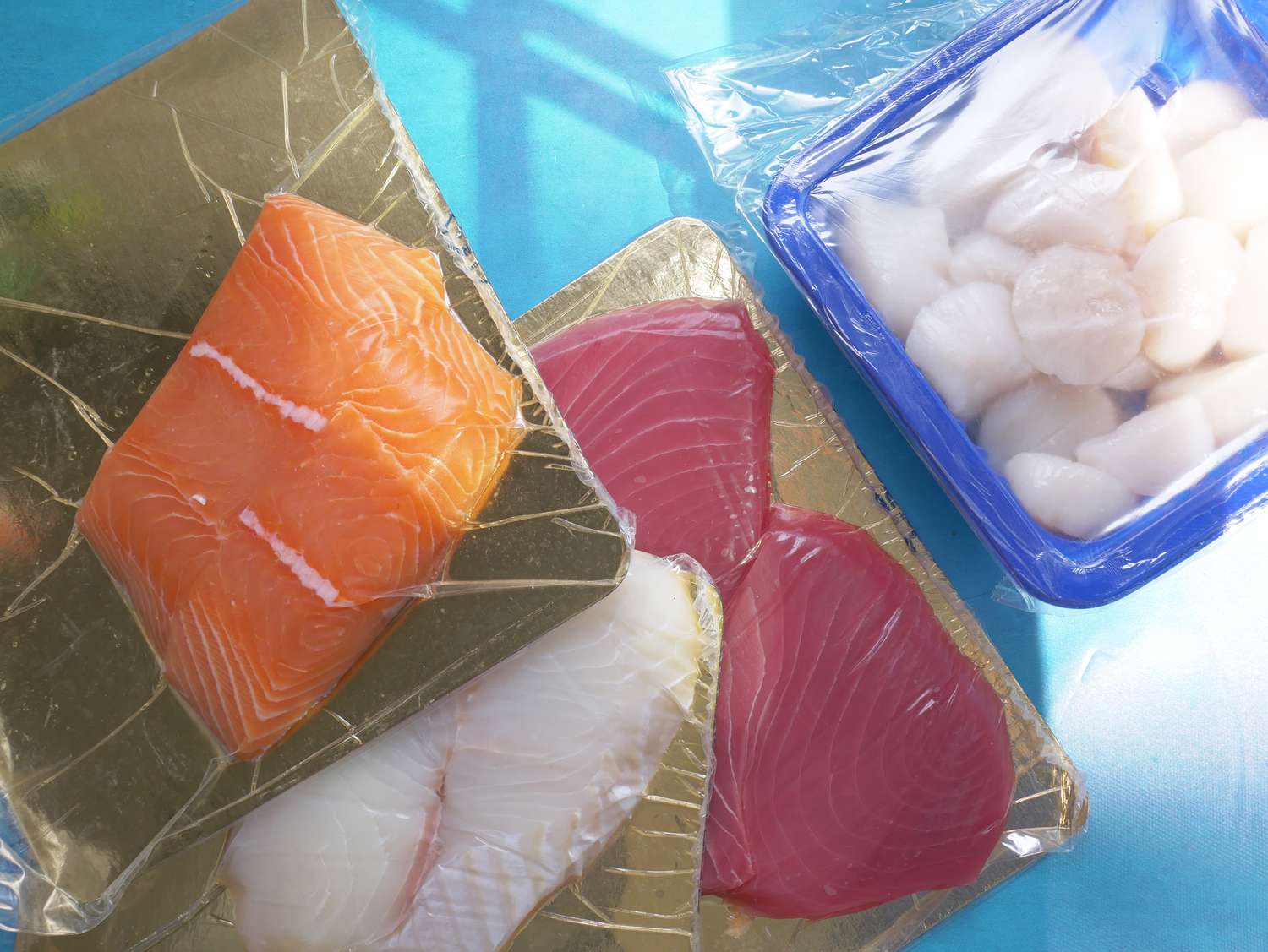 A few packages of fish fillets and a container of scallops on a blue surface