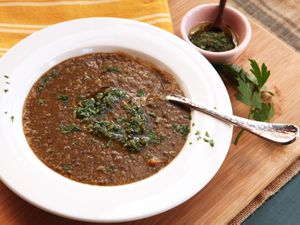 A big bowl of lentil soup, topped with gremolata, next to a small bowl of gremolata with olive oil for topping.