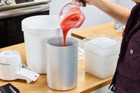 A person pouring red liquid into the metal canister of the Hamilton Beach Automatic Ice Cream Maker