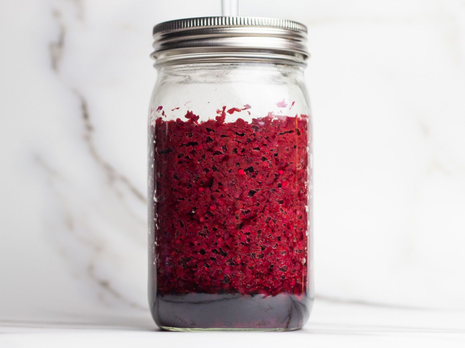 Profile view of a mason jar with the fermenting pepper-berry mash. The mixture has separated somewhat and changed color.