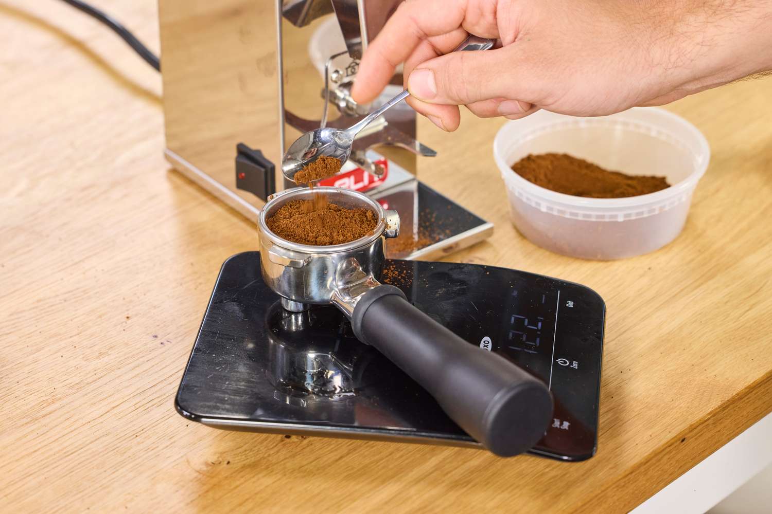 A hand adding ground coffee into a portafilter made in the Lelit Fred Tempo Burr Grinder