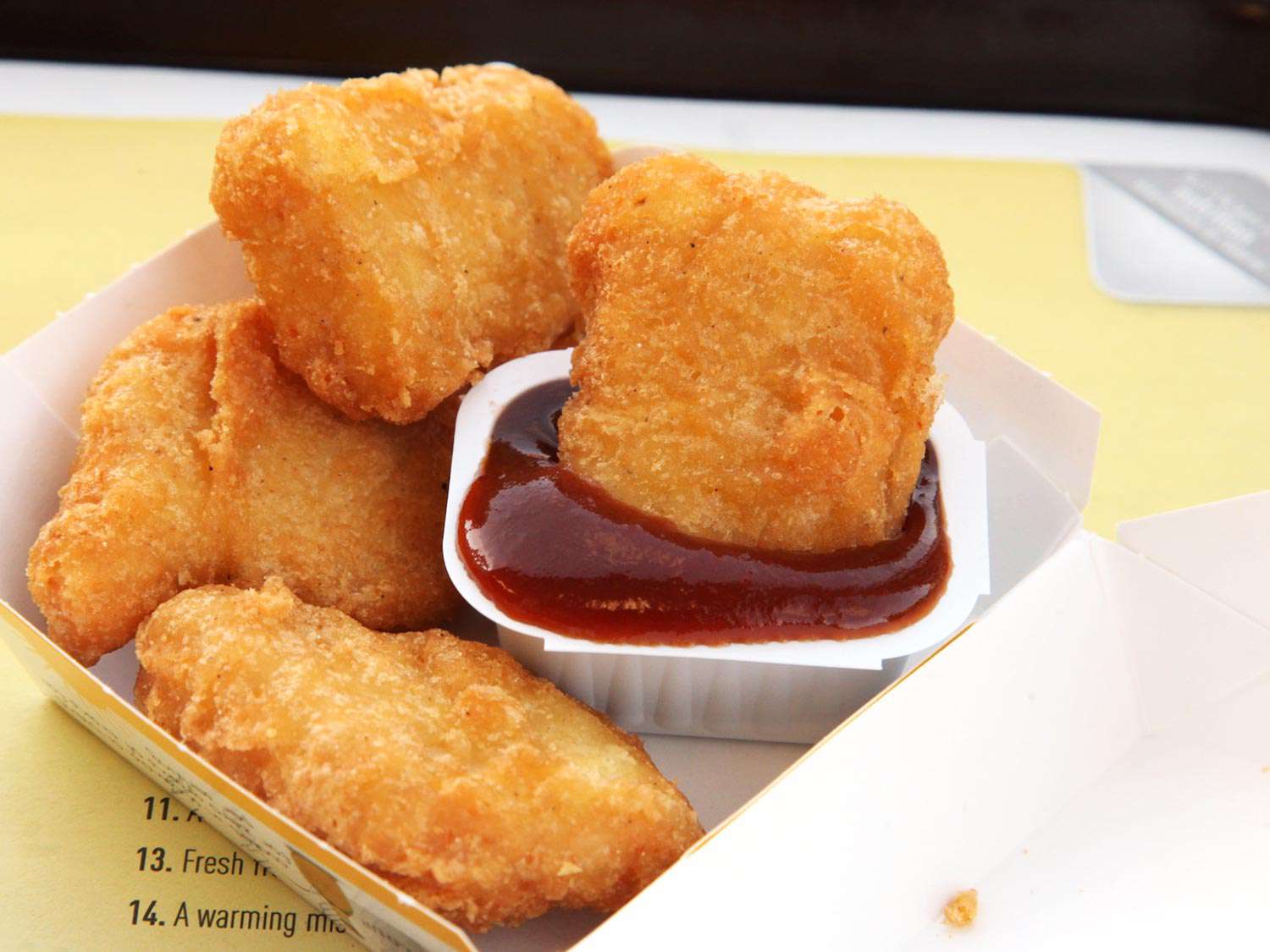 A box of chicken McNuggets from McDonald's with one nugget dipped in a container of sauce