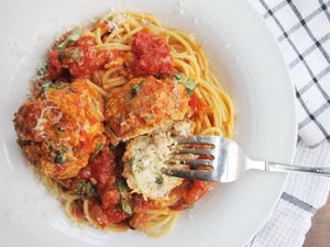 Overhead view of a white bowl of spaghetti topped with parmesan chicken meatballs.