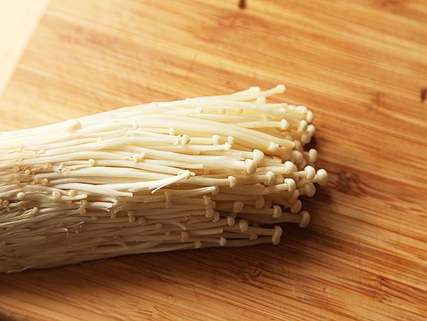 Enoki mushroom resting on a cutting board.
