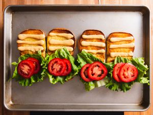Four toasted burger buns open on a baking sheet, each one with three lines of homemade Shack Sauce on the top half of the bun, and lettuce and tomato on the bottom half of the bun.