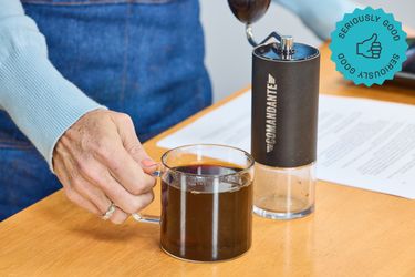 the comandante hand grinder with a cup of coffee next to it