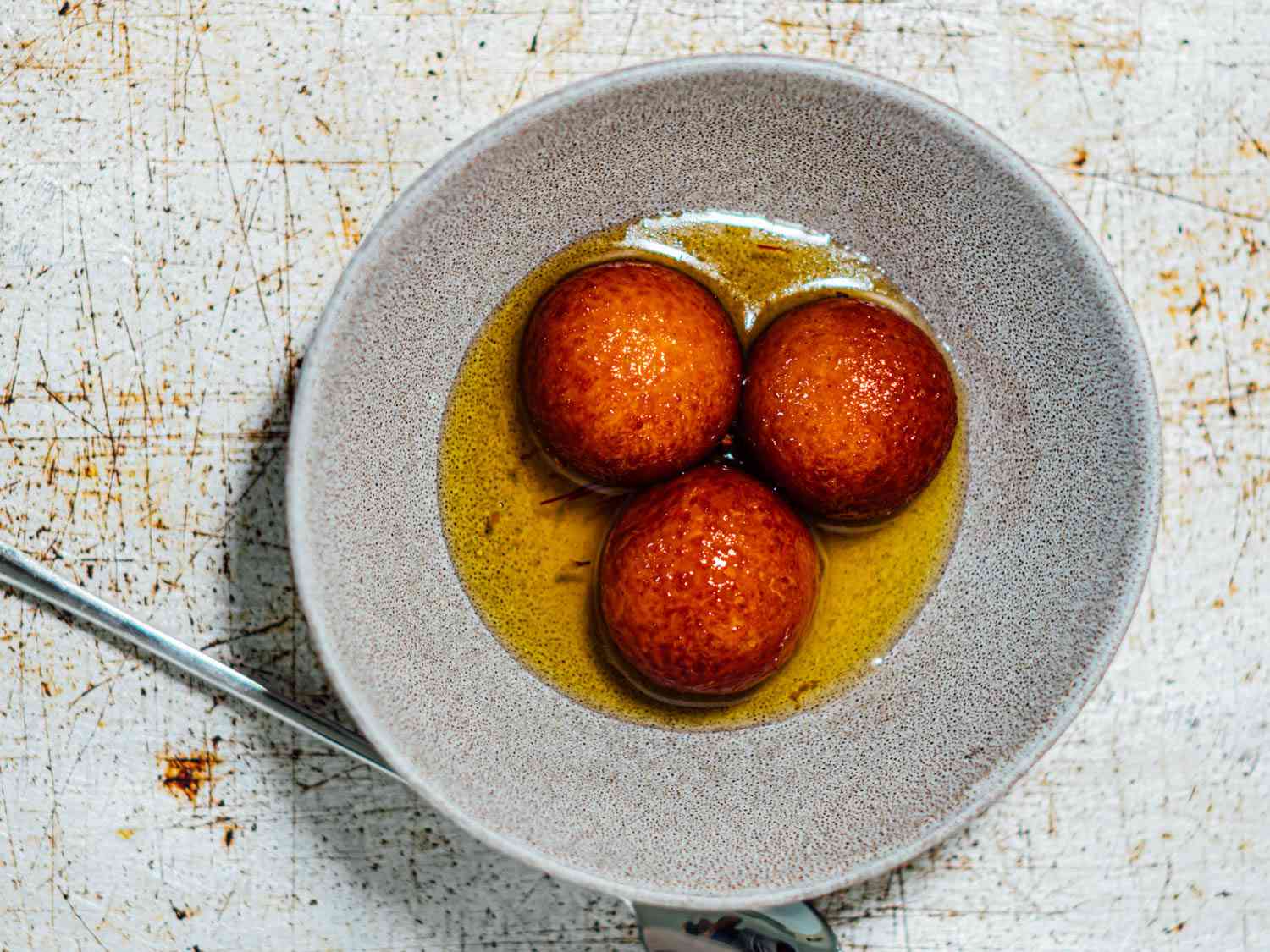 Three golden brown gulab jamuns soaking in syrup in a grey bowl.