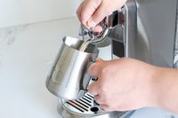 A person steaming milk using a metal pitcher and an espresso machine