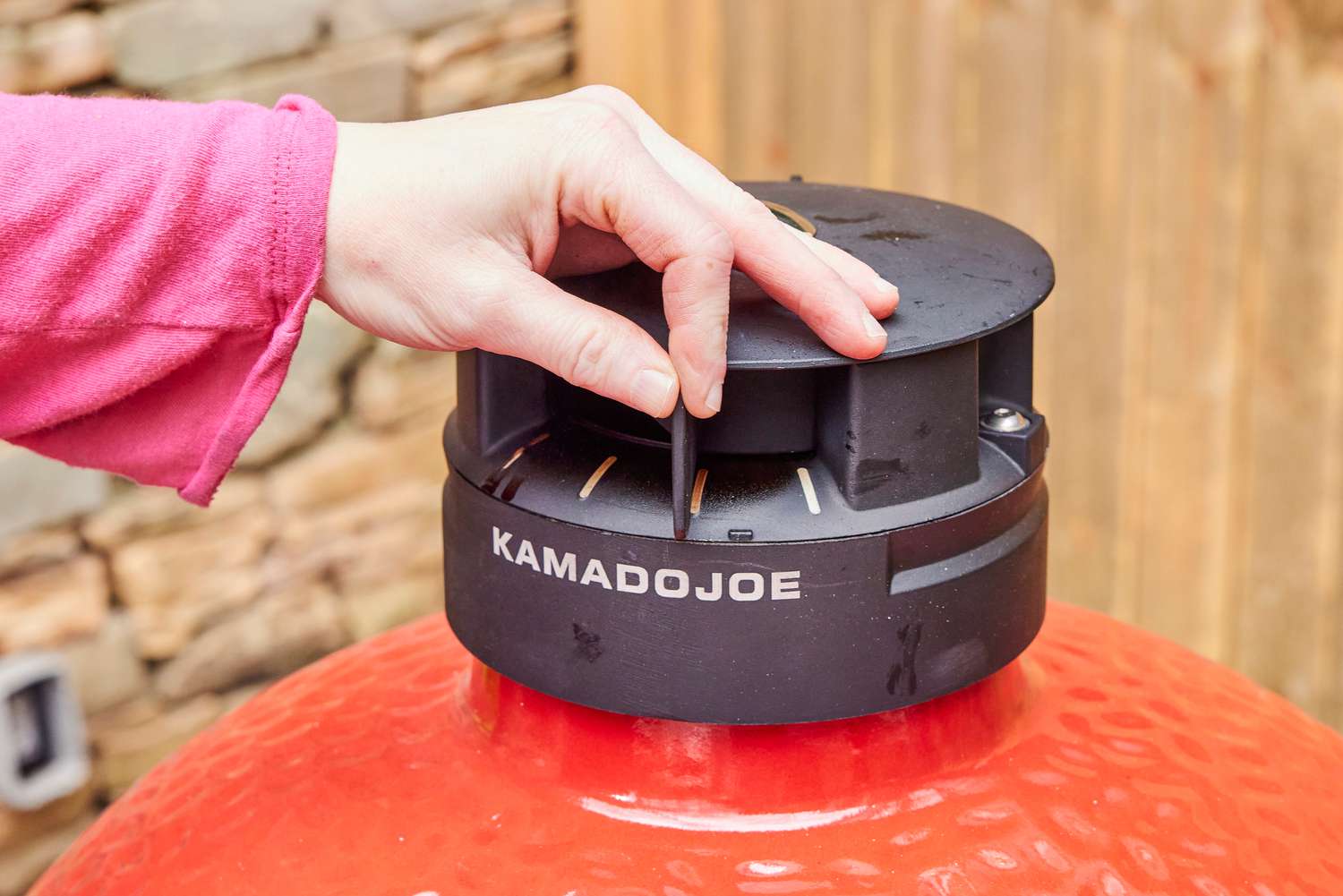 A person opens a vent on the Kamado Joe Classic II Charcoal Grill