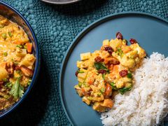 Overhead view of a portion of vegetable qorma served next to white rice on a blue plate, on a textured blue fabric