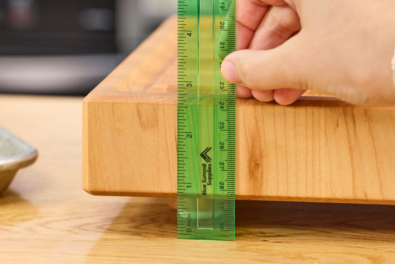 A hand measuring the thickness of a Boardsmith Maple End-Grain Cutting Board with a green ruler