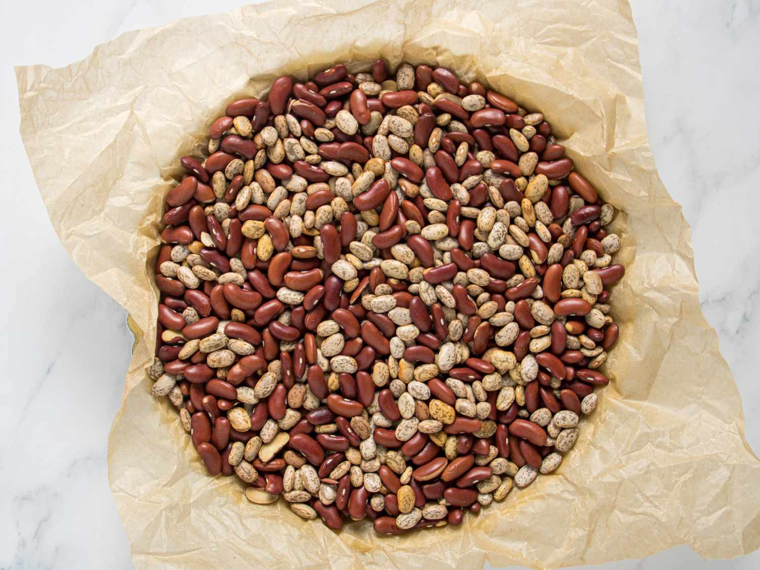 Beans and parchment paper covering a pate brisee on a marble surface 