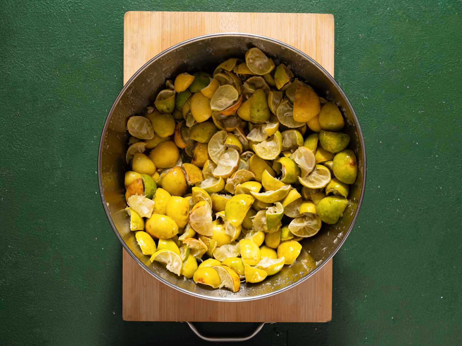 A pot filled with used lemon halves placed on a wooden board